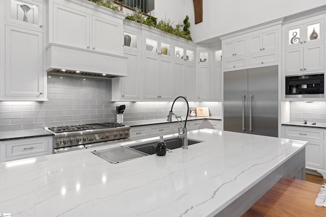 kitchen featuring white cabinets, decorative backsplash, custom range hood, glass insert cabinets, and appliances with stainless steel finishes