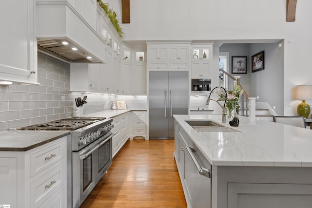 kitchen featuring an island with sink, high quality appliances, custom exhaust hood, light wood-type flooring, and a sink