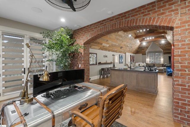 office space featuring arched walkways, brick wall, light wood finished floors, and lofted ceiling