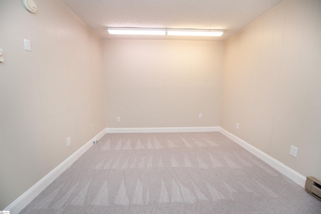 spare room featuring a baseboard heating unit, a textured ceiling, light carpet, and baseboards