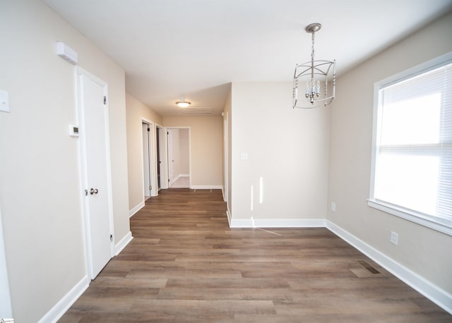 unfurnished dining area with visible vents, a notable chandelier, baseboards, and wood finished floors