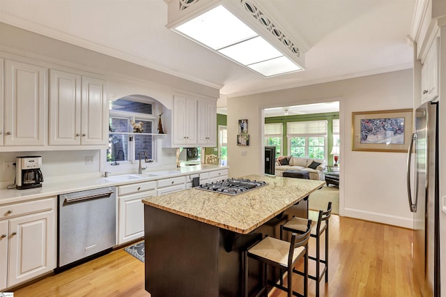 kitchen with appliances with stainless steel finishes, a kitchen bar, white cabinets, and crown molding