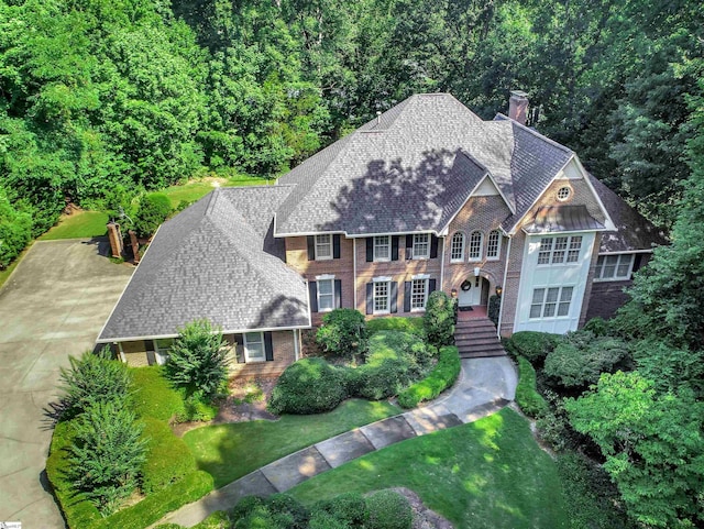 view of front facade featuring a shingled roof, a front yard, brick siding, and a chimney