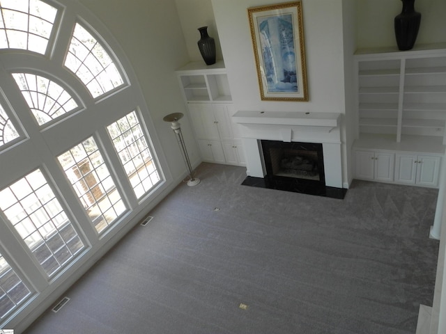 unfurnished living room featuring built in shelves, light colored carpet, visible vents, a towering ceiling, and a fireplace with flush hearth