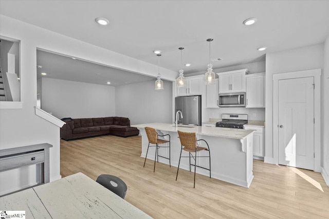 kitchen with a kitchen island with sink, stainless steel appliances, light wood-style floors, white cabinets, and a kitchen bar