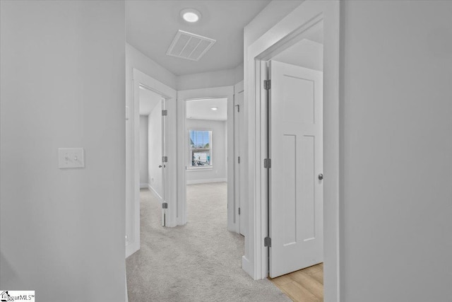 hallway with light carpet, baseboards, and visible vents