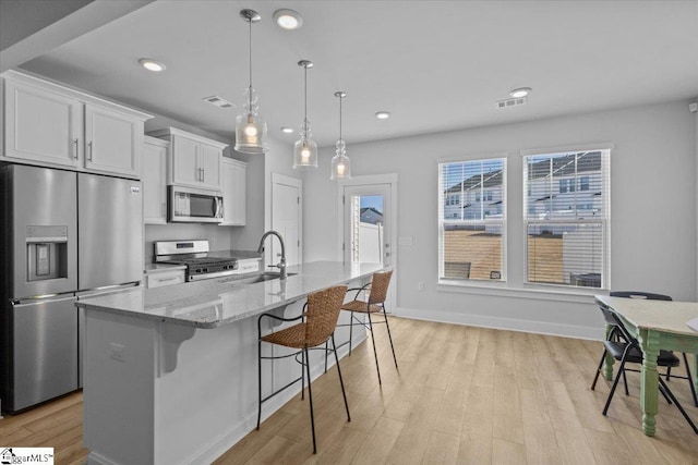 kitchen featuring light stone counters, a breakfast bar area, stainless steel appliances, visible vents, and white cabinetry