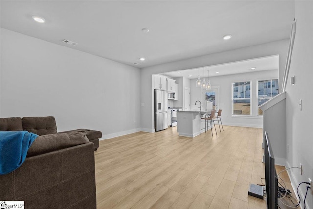 living room featuring light wood finished floors, baseboards, visible vents, and recessed lighting