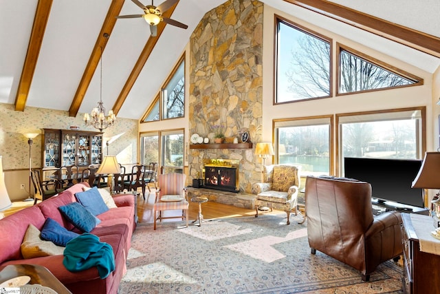 living area with wood finished floors, beamed ceiling, a stone fireplace, high vaulted ceiling, and ceiling fan with notable chandelier