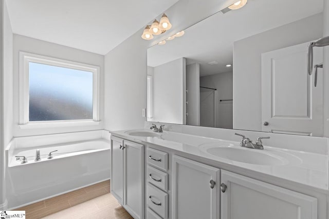 full bath featuring wood finished floors, a sink, a bath, and double vanity