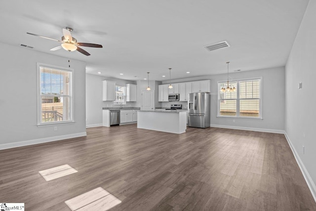 unfurnished living room with a healthy amount of sunlight, visible vents, and ceiling fan with notable chandelier