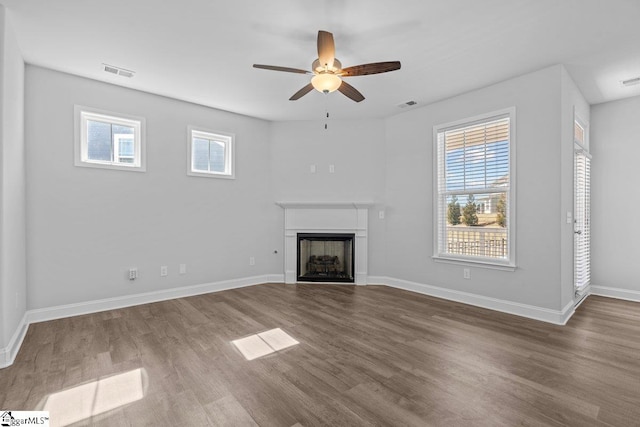 unfurnished living room with a fireplace, wood finished floors, visible vents, and baseboards