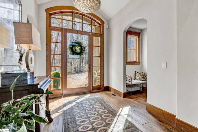 foyer with baseboards, arched walkways, lofted ceiling, wood-type flooring, and a chandelier