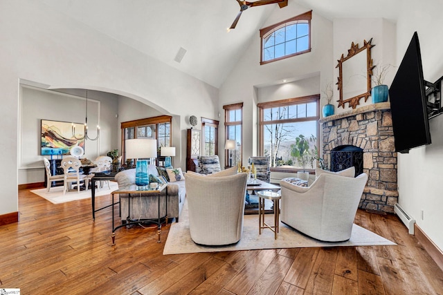 living room with ceiling fan with notable chandelier, hardwood / wood-style floors, a baseboard radiator, and a fireplace