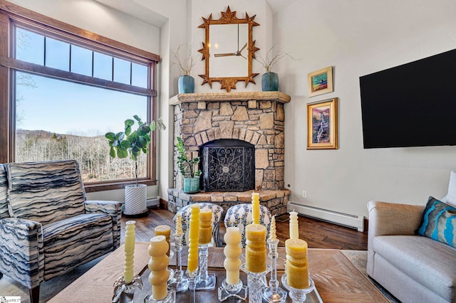 living area with a healthy amount of sunlight, a baseboard radiator, wood finished floors, and a stone fireplace