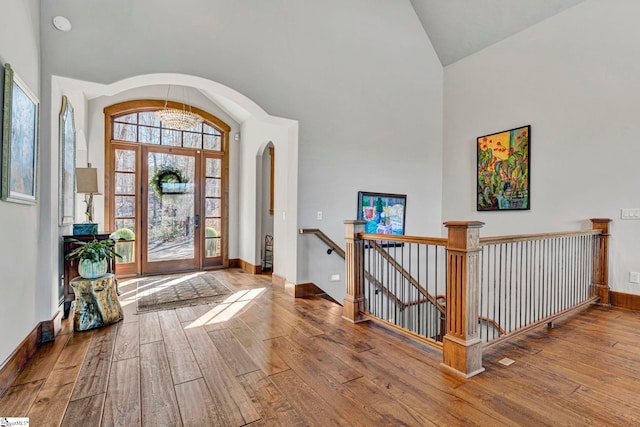 foyer entrance featuring hardwood / wood-style flooring, baseboards, arched walkways, and high vaulted ceiling