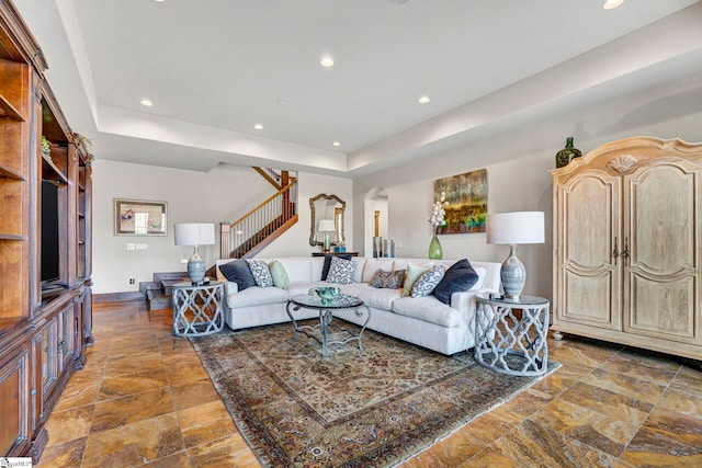 living room featuring arched walkways, a tray ceiling, recessed lighting, stairway, and stone finish floor