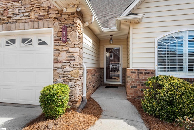 entrance to property featuring a garage, stone siding, and roof with shingles