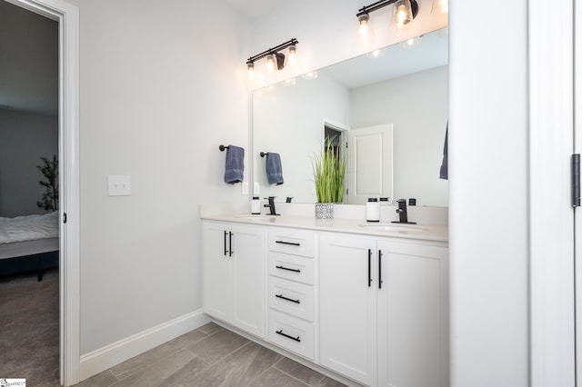 full bathroom with double vanity, ensuite bath, a sink, and baseboards