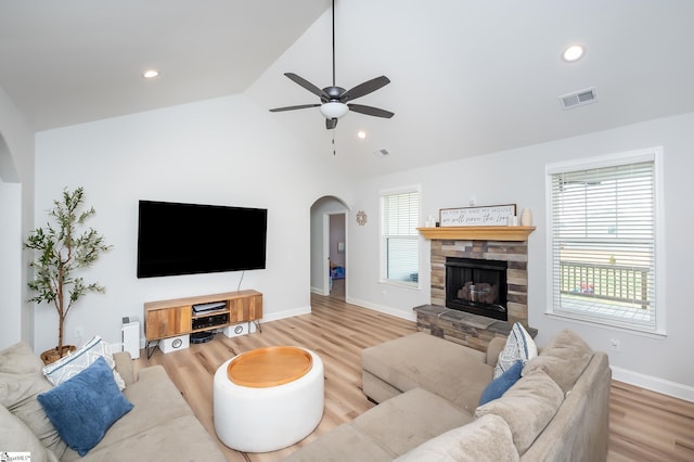 living area with arched walkways, a stone fireplace, wood finished floors, visible vents, and vaulted ceiling