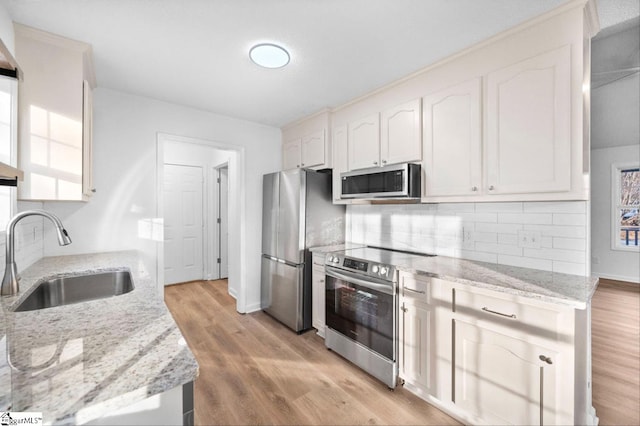 kitchen featuring appliances with stainless steel finishes, a sink, light wood-style floors, and tasteful backsplash