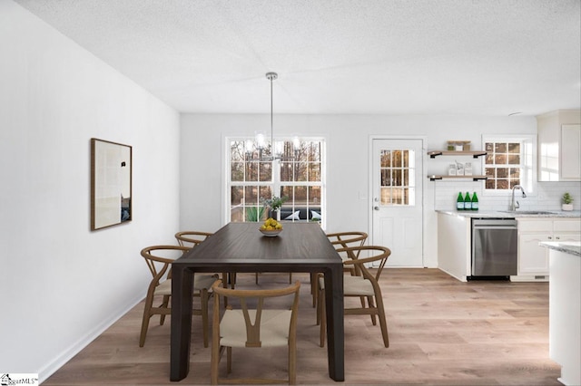 dining room with a textured ceiling, light wood finished floors, a chandelier, and baseboards