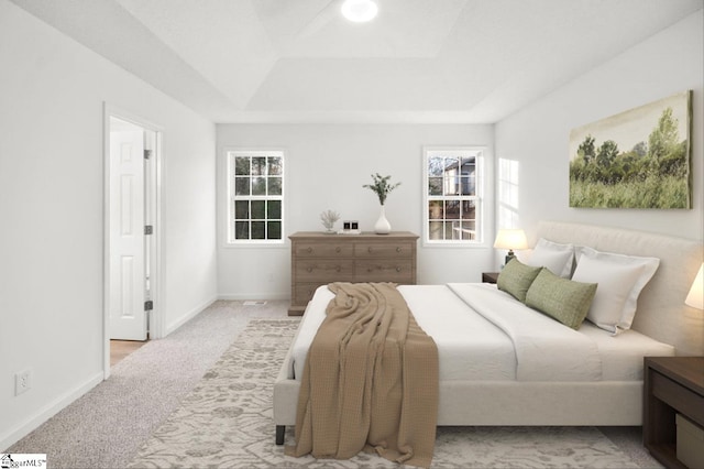 carpeted bedroom with multiple windows, a raised ceiling, and baseboards