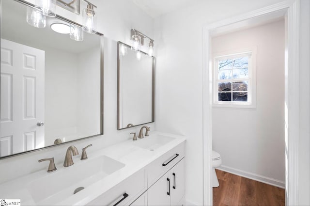 bathroom featuring double vanity, a sink, toilet, and wood finished floors