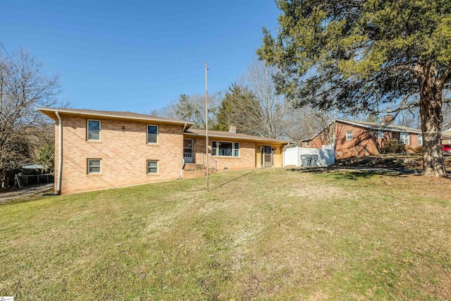 back of house with brick siding, a yard, a chimney, and fence