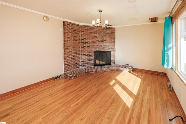 unfurnished living room featuring a brick fireplace, a notable chandelier, crown molding, and wood finished floors