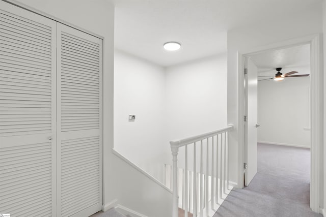 hallway featuring carpet, baseboards, and an upstairs landing