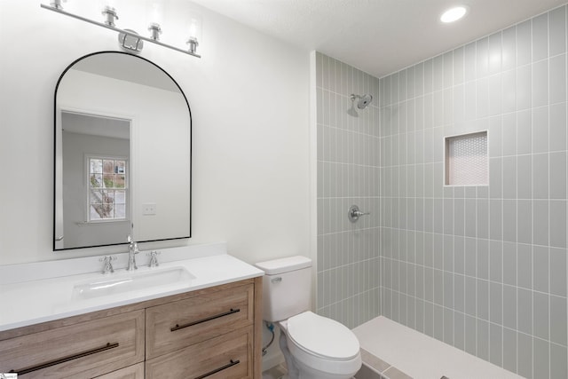 full bath featuring vanity, a tile shower, and toilet