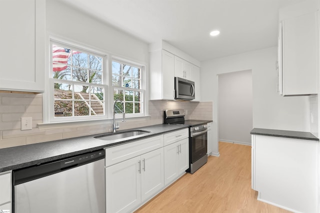 kitchen with dark countertops, white cabinets, stainless steel appliances, and a sink