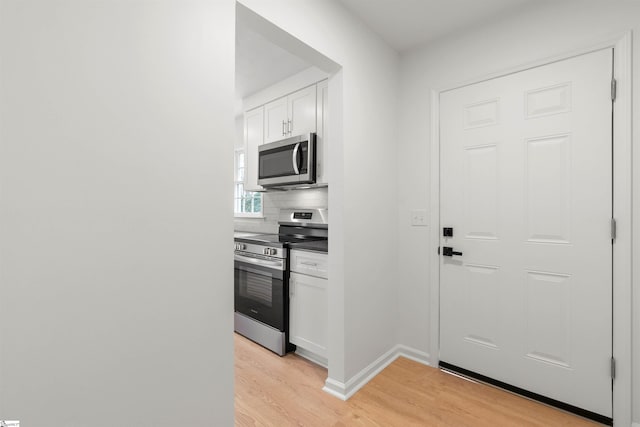 kitchen featuring decorative backsplash, appliances with stainless steel finishes, white cabinets, light wood-type flooring, and baseboards