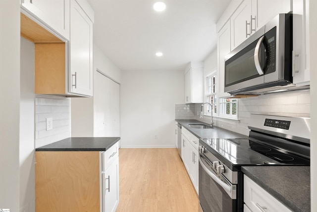 kitchen featuring dark countertops, light wood-style flooring, appliances with stainless steel finishes, a sink, and backsplash