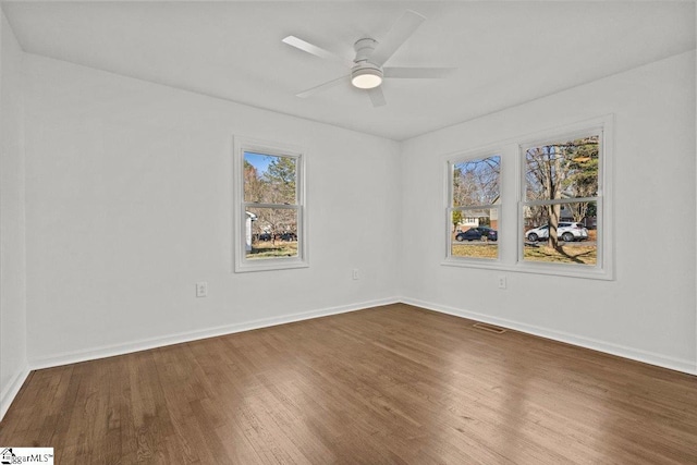 spare room with dark wood-style floors, visible vents, baseboards, and a ceiling fan