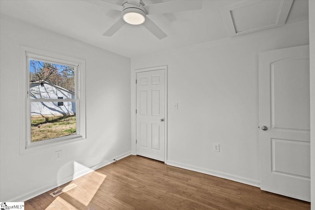 unfurnished bedroom with ceiling fan, wood finished floors, visible vents, baseboards, and attic access