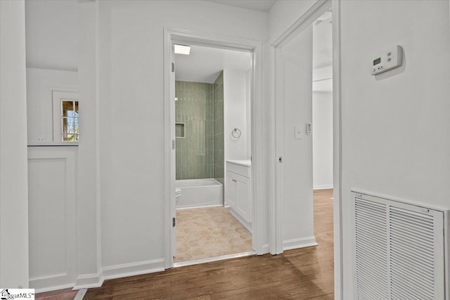 hallway with baseboards, visible vents, and wood finished floors