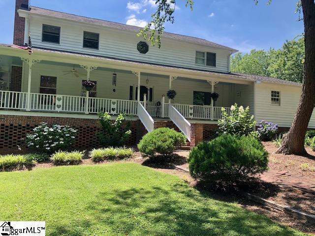 farmhouse-style home featuring covered porch, a chimney, a front lawn, and stairs