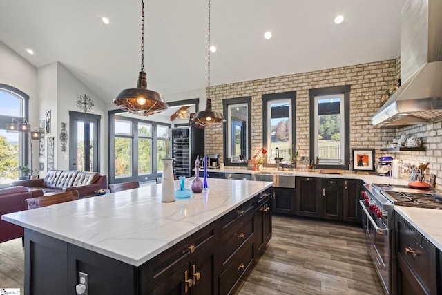 kitchen featuring a sink, open floor plan, wall chimney range hood, high end stainless steel range oven, and light stone countertops