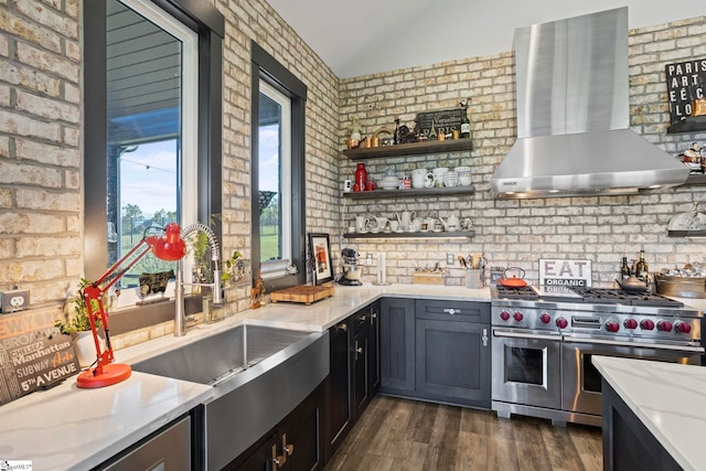 kitchen with lofted ceiling, brick wall, wall chimney range hood, double oven range, and dark wood finished floors