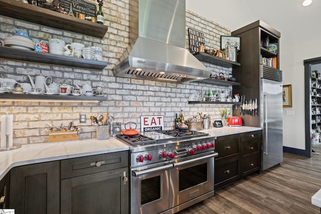 kitchen featuring premium appliances, light stone counters, dark wood finished floors, open shelves, and wall chimney range hood