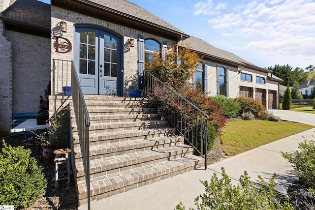 view of front of property with a shingled roof, french doors, brick siding, and driveway