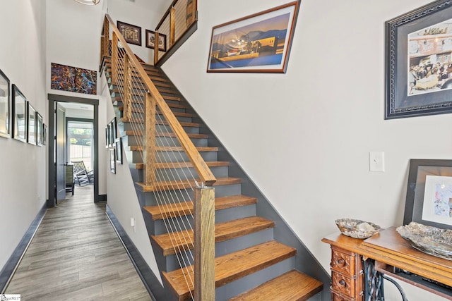 stairs with a high ceiling, baseboards, and wood finished floors