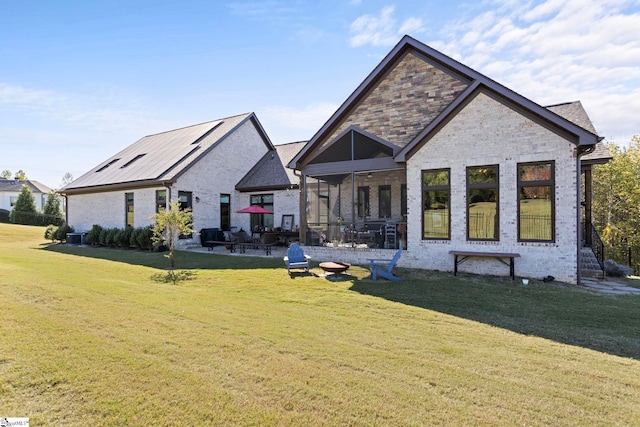 rear view of property with brick siding, a sunroom, a yard, stone siding, and a patio area