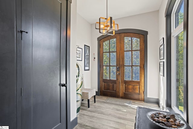 foyer featuring arched walkways, french doors, a chandelier, and light wood-style flooring