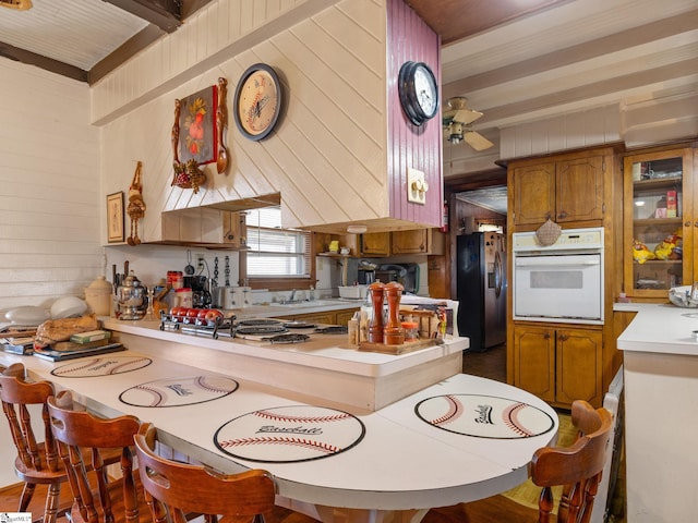 kitchen featuring white oven, brown cabinets, light countertops, a peninsula, and stainless steel fridge with ice dispenser