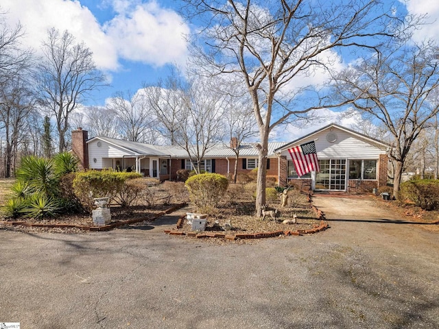 ranch-style house with brick siding, driveway, and a chimney