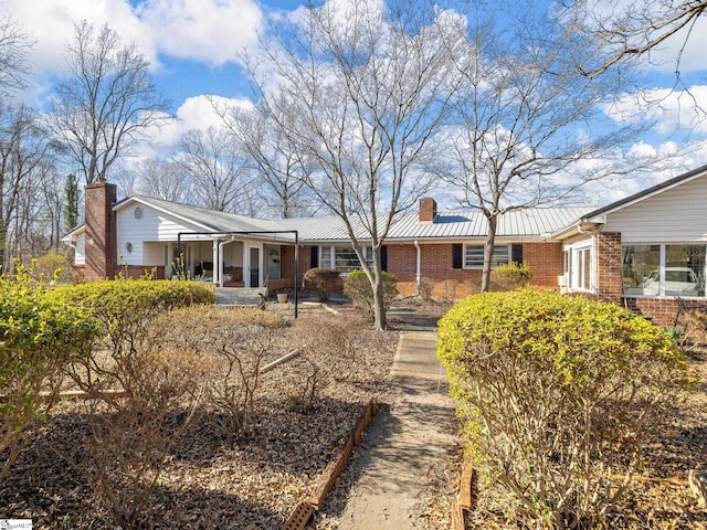 view of front of home featuring covered porch, brick siding, metal roof, and a chimney