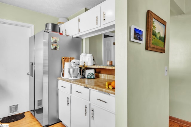 kitchen with light wood-type flooring, white cabinets, light countertops, and stainless steel fridge with ice dispenser